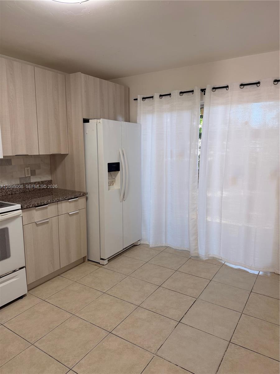 Kitchen with light wood cabinets, a white side-by-side refrigerator, and white curtains.