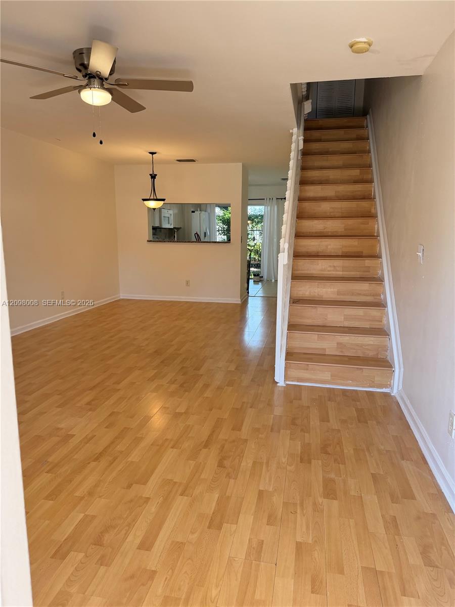 Empty living room with light wood flooring, a ceiling fan, and stairs to the upper level.