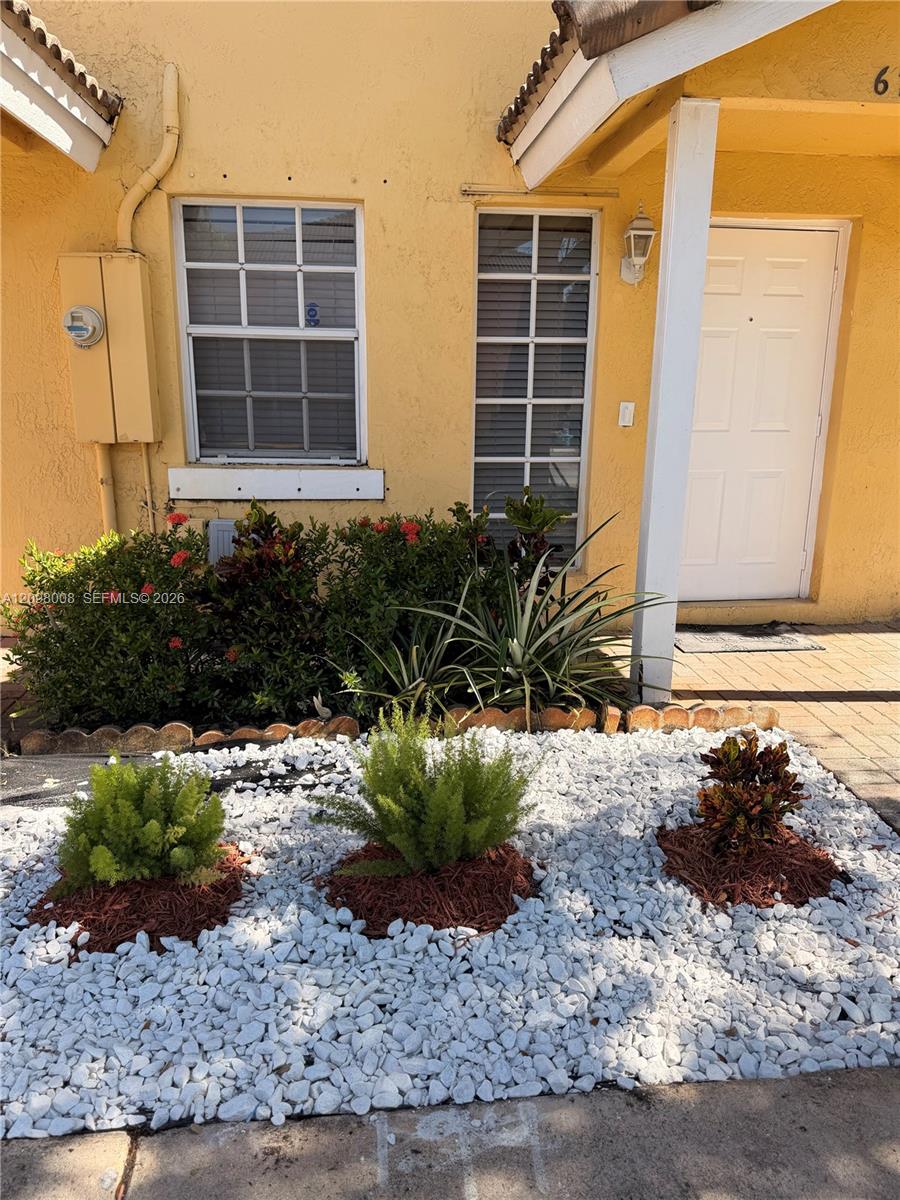 Yellow stucco home with a white entry door and a front garden of white stones and shrubs.