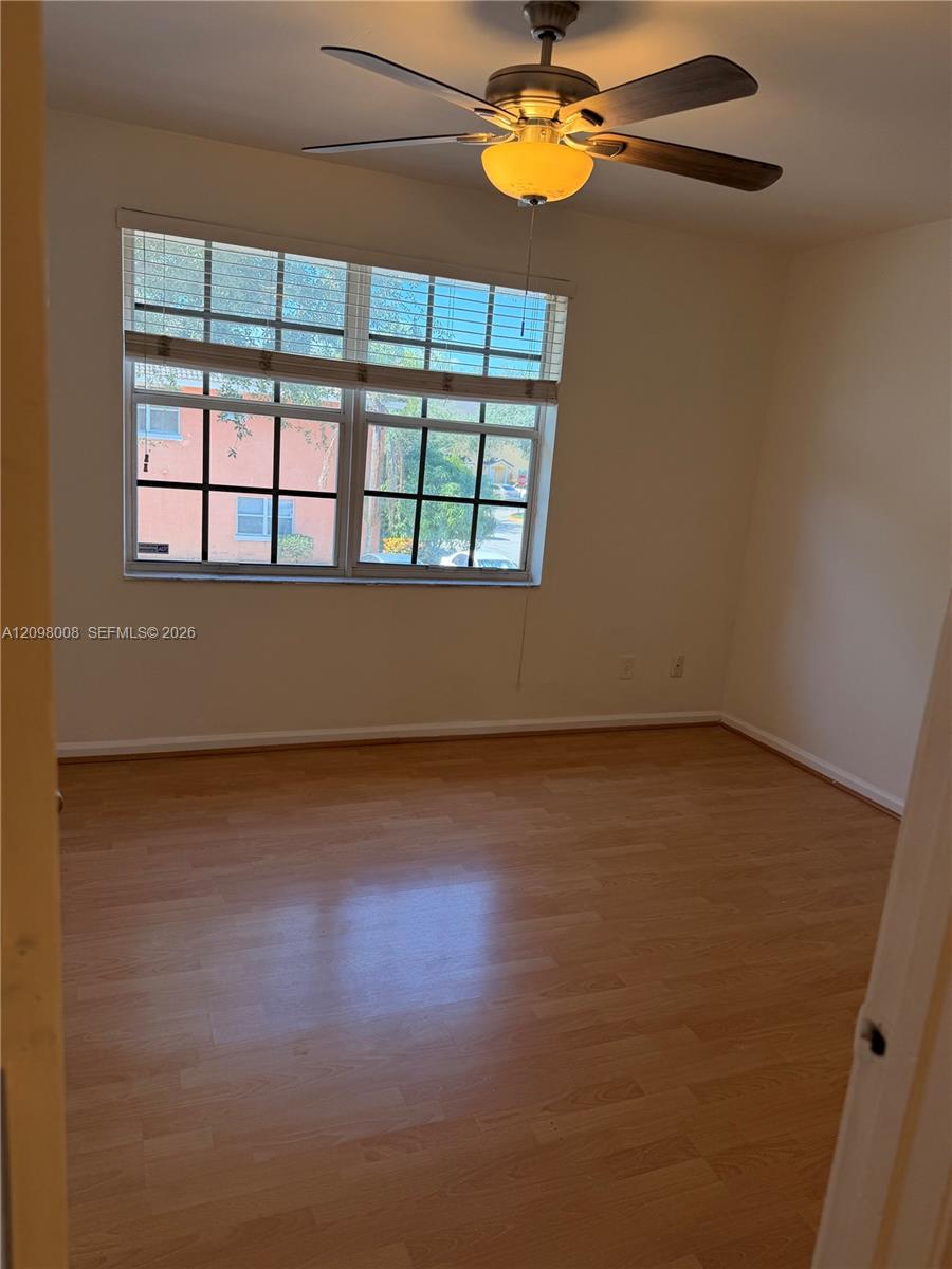 Empty bedroom with wood flooring, a ceiling fan, and a large gridded window.