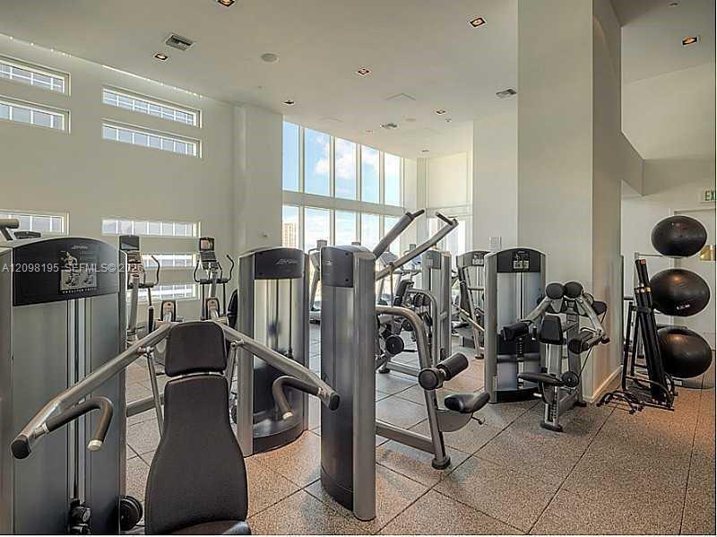 Condominium fitness center with rows of exercise machines beneath tall windows.