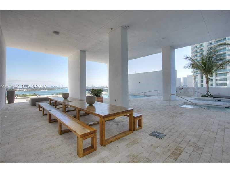Covered terrace with a long wooden picnic table, pool area, and waterfront skyline views.