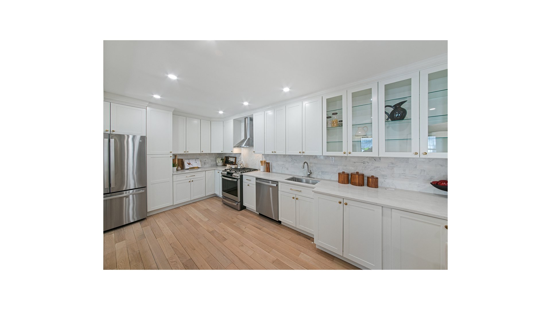 Bright kitchen with white cabinetry, marble backsplash, stainless steel appliances, and wide-plank wood flooring.