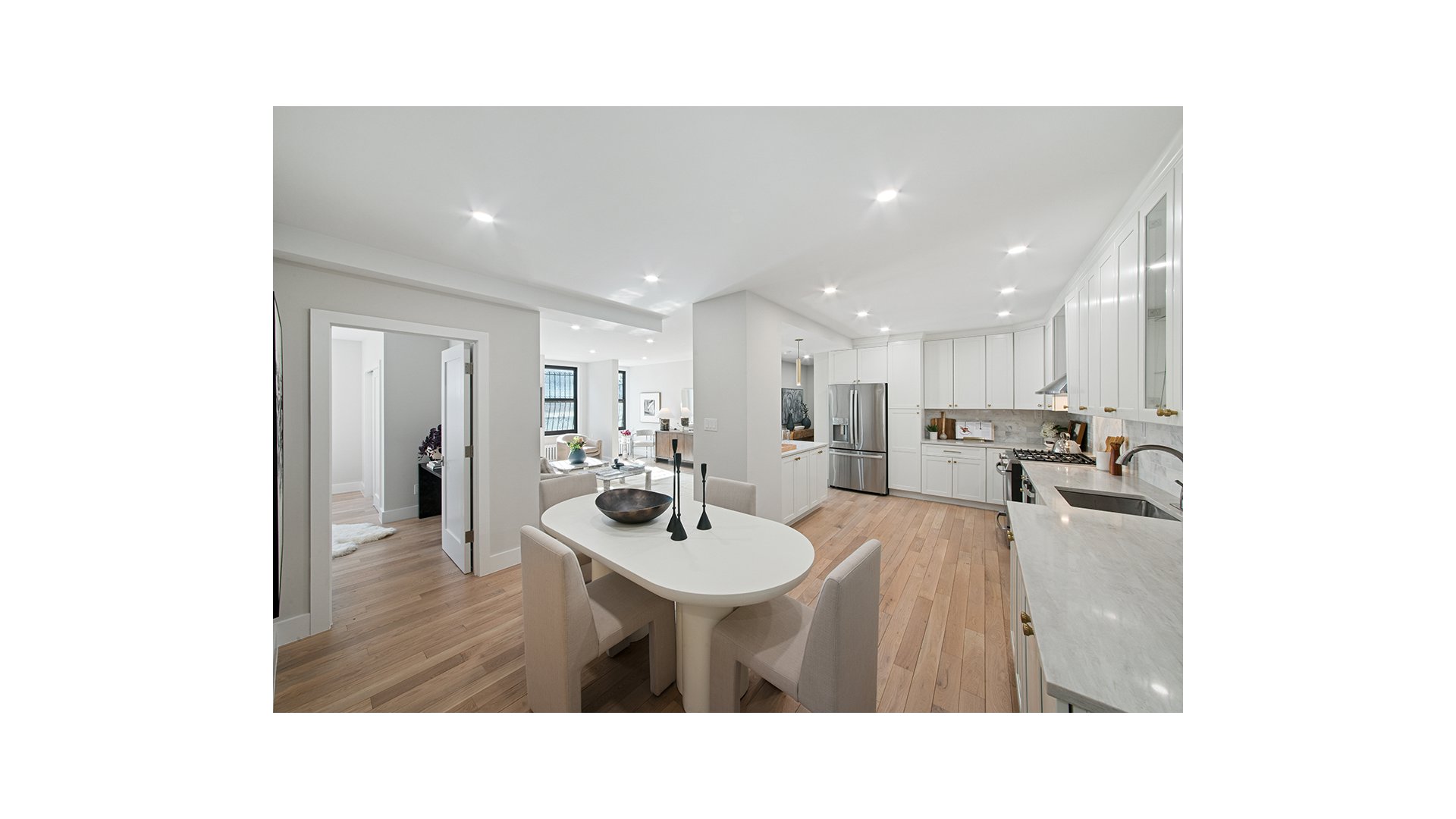 Open kitchen and dining area with white cabinetry, marble counters, and a long oval dining table.