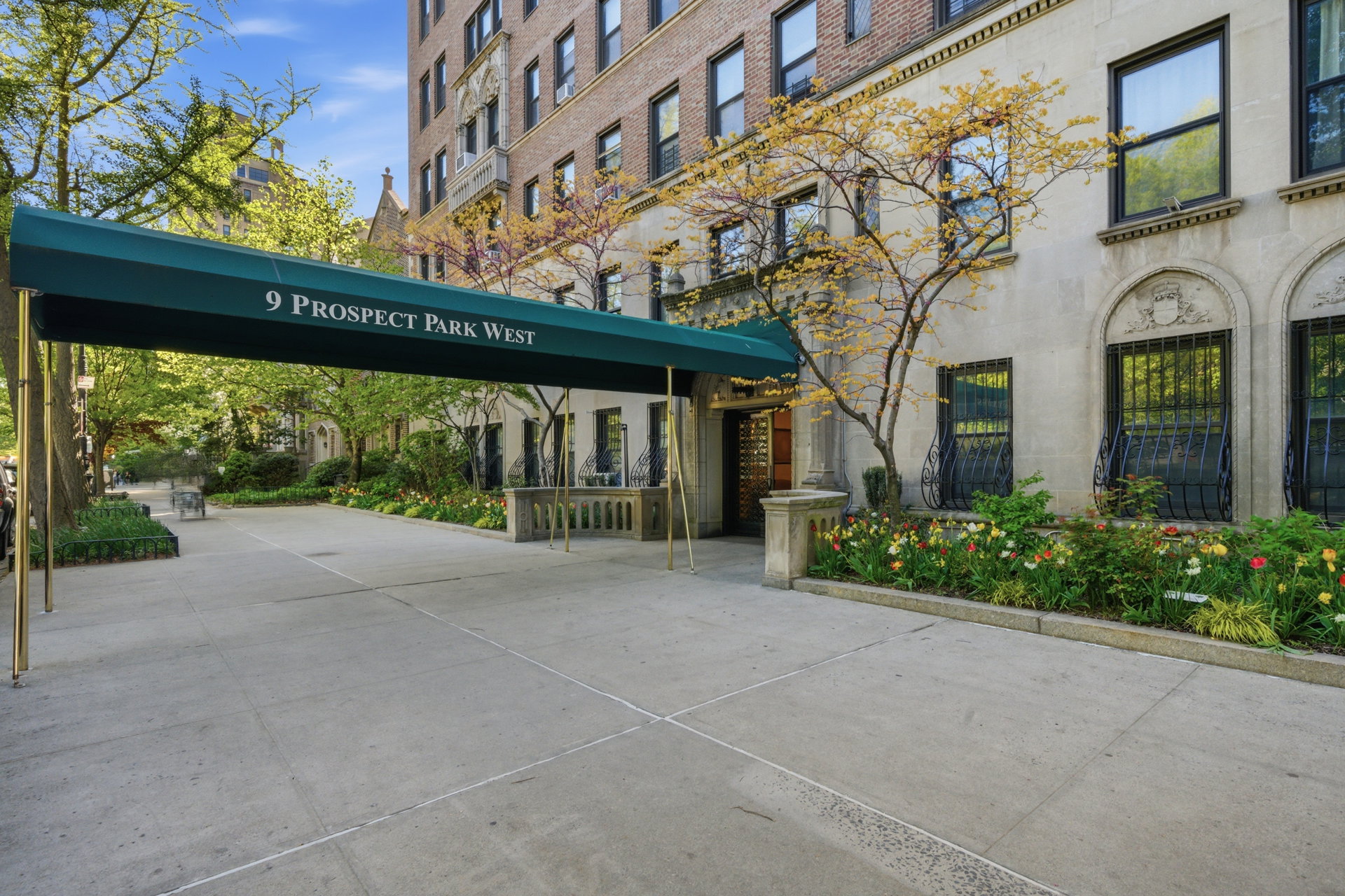 Entrance to 9 Prospect Park West beneath a green canopy, beside landscaped flower beds.