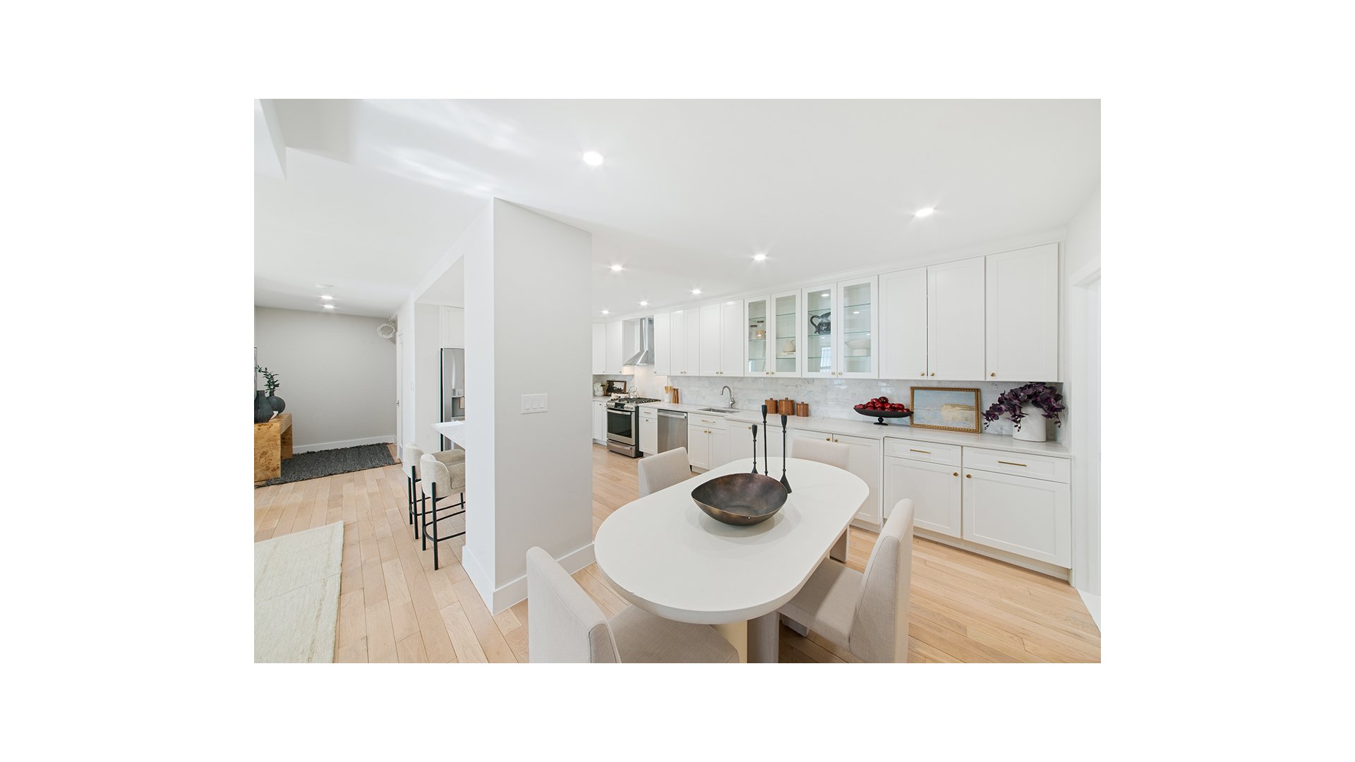 Bright white kitchen with glass-front cabinets and an oval dining table.