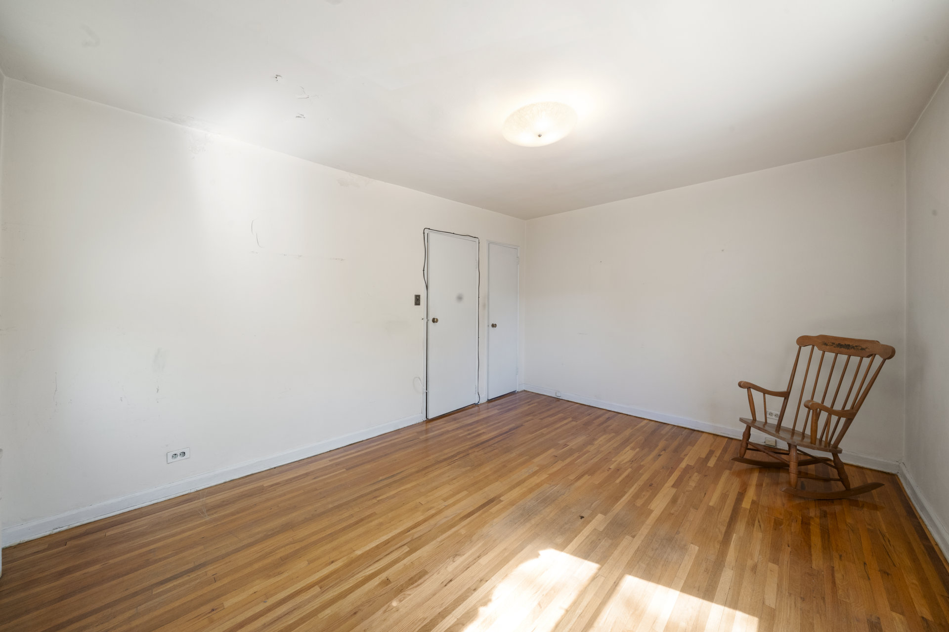 Nearly empty room with hardwood floors, white walls, and a wooden rocking chair.