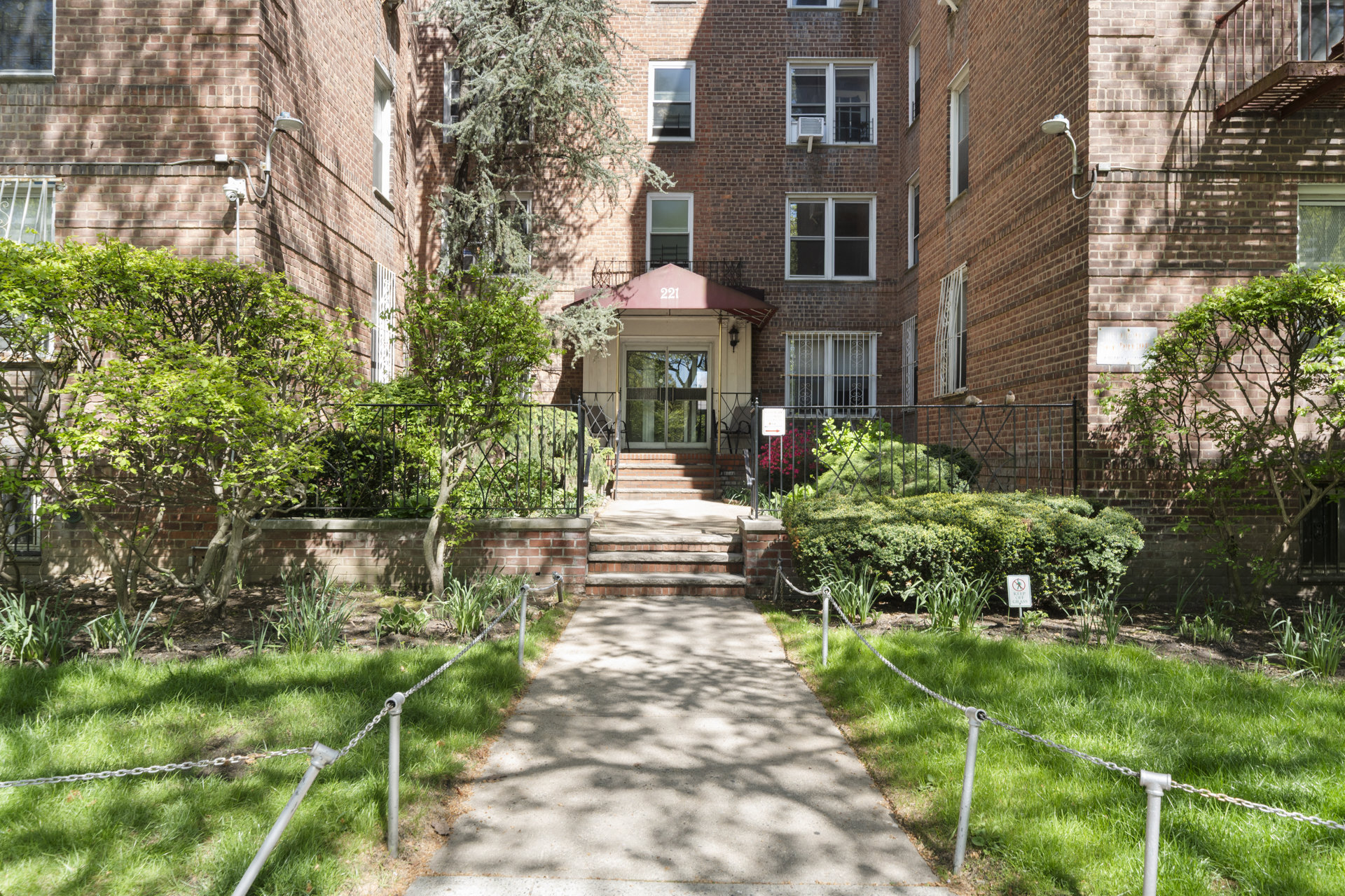 Brick apartment building entrance at 221, approached by a landscaped walkway and steps.