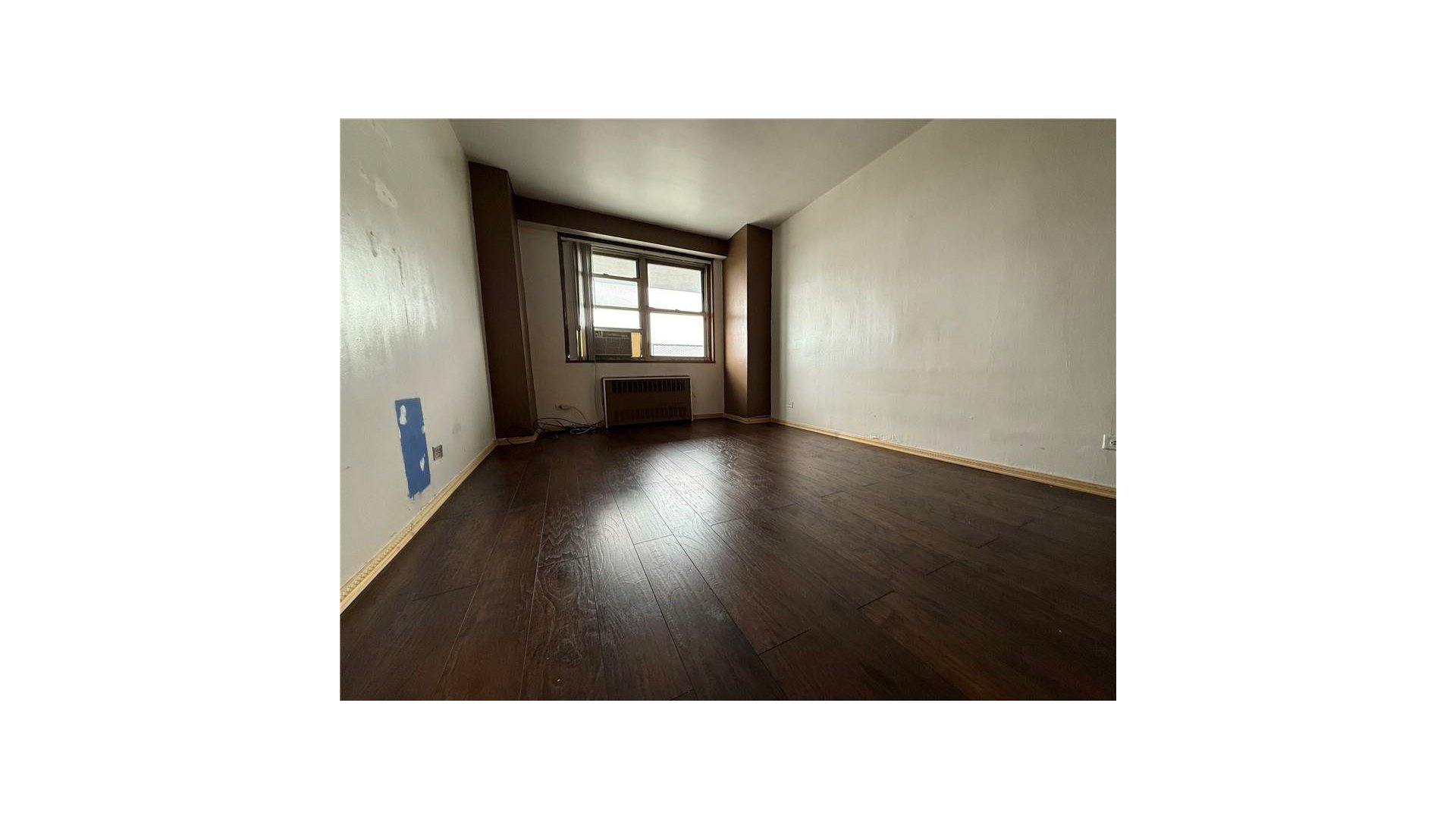 Vacant room with dark wood floors, a window air conditioner, and radiator.