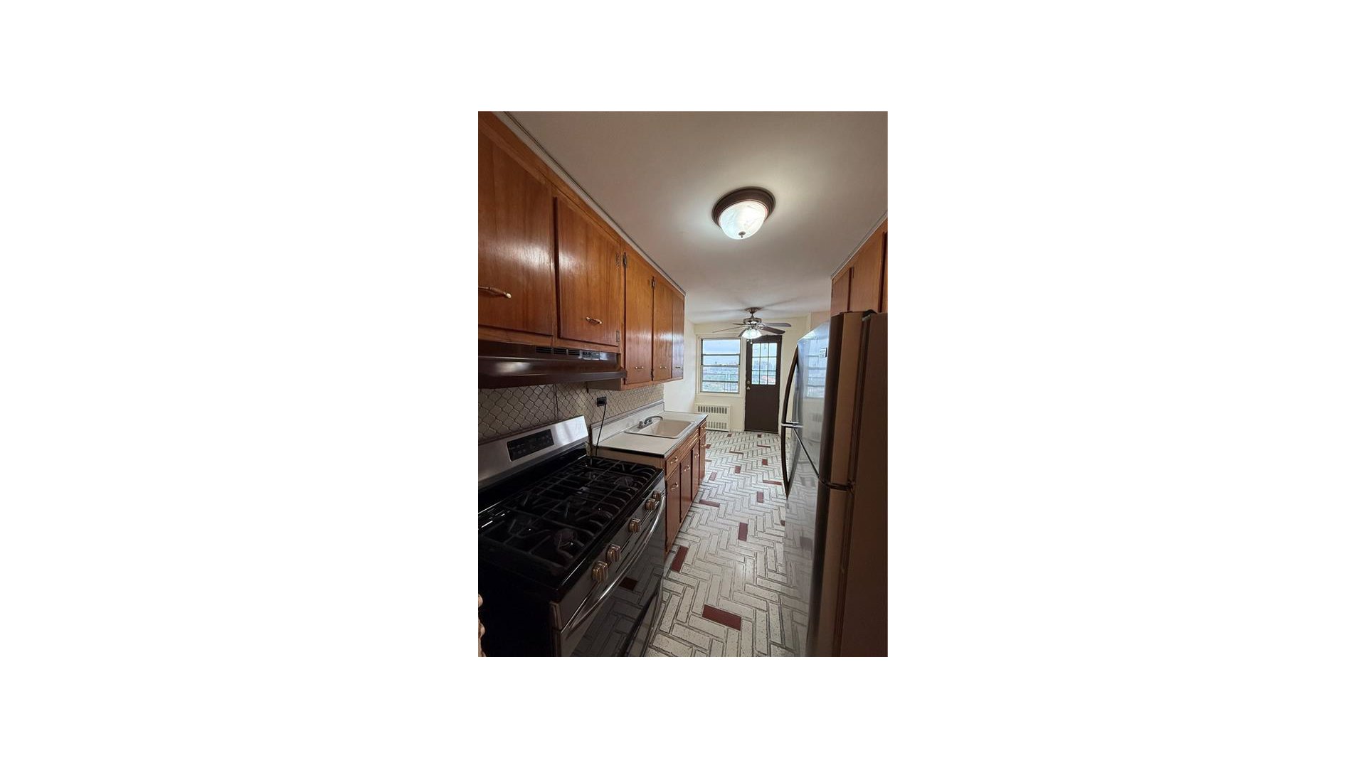 Galley kitchen with wood cabinets, a gas range, and a window at the far end.