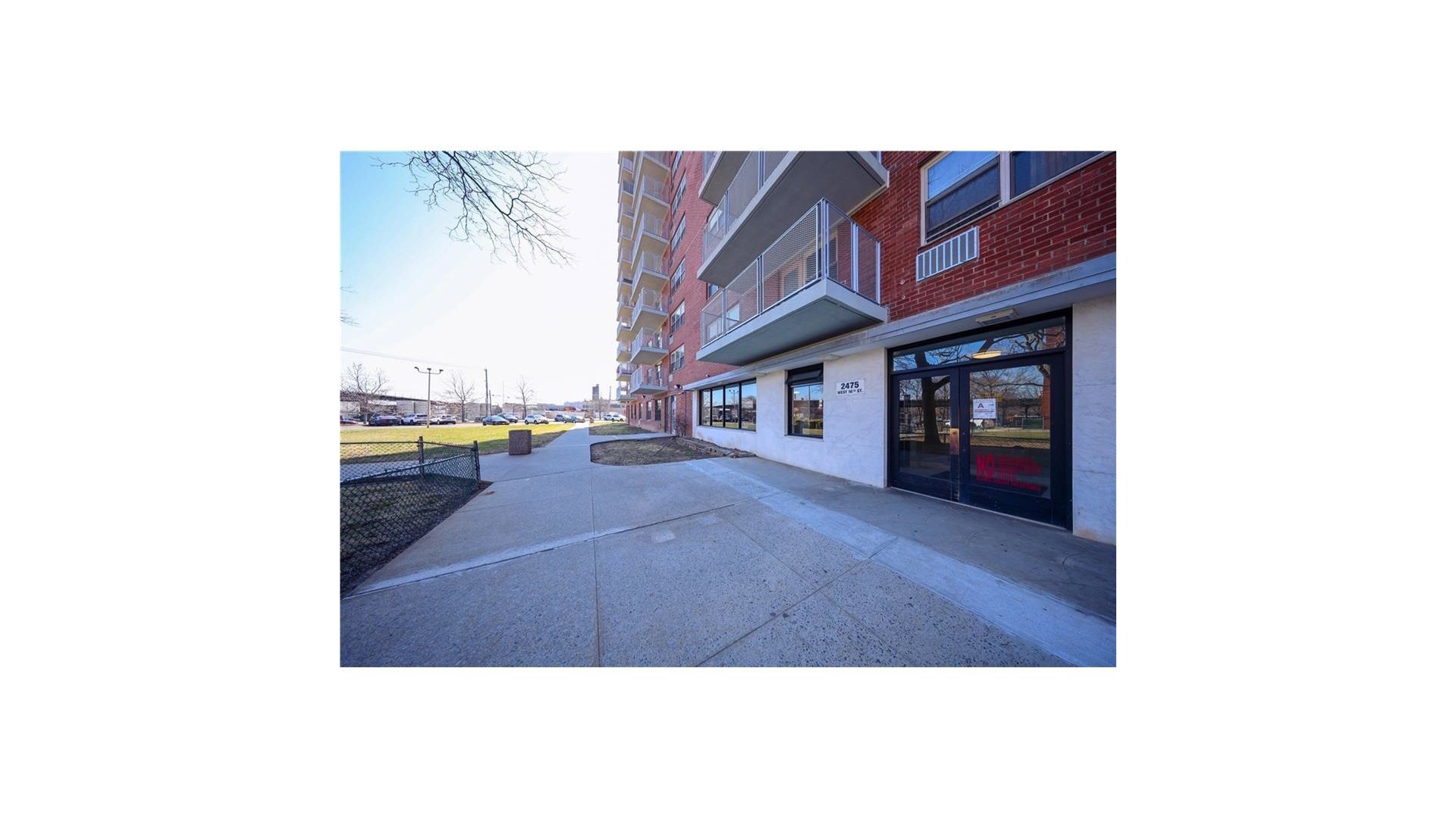 Brick apartment building entrance with projecting balconies and a broad concrete sidewalk.