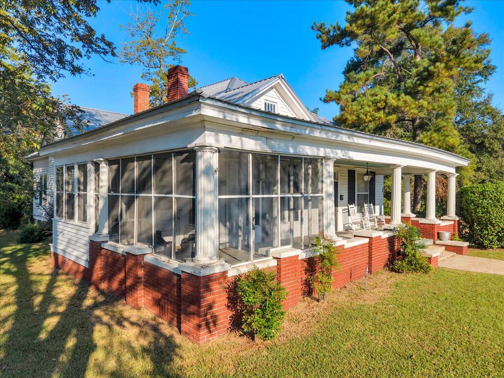 White house with a broad screened porch, white columns, and a red brick foundation.