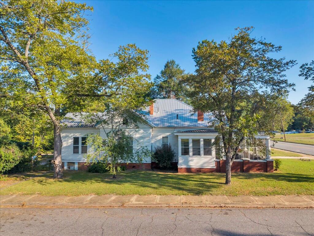 White house with a metal roof and enclosed porch, shaded by mature trees.