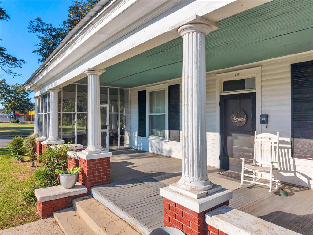 White house front porch with fluted columns on brick bases, screened section, and rocking chairs.