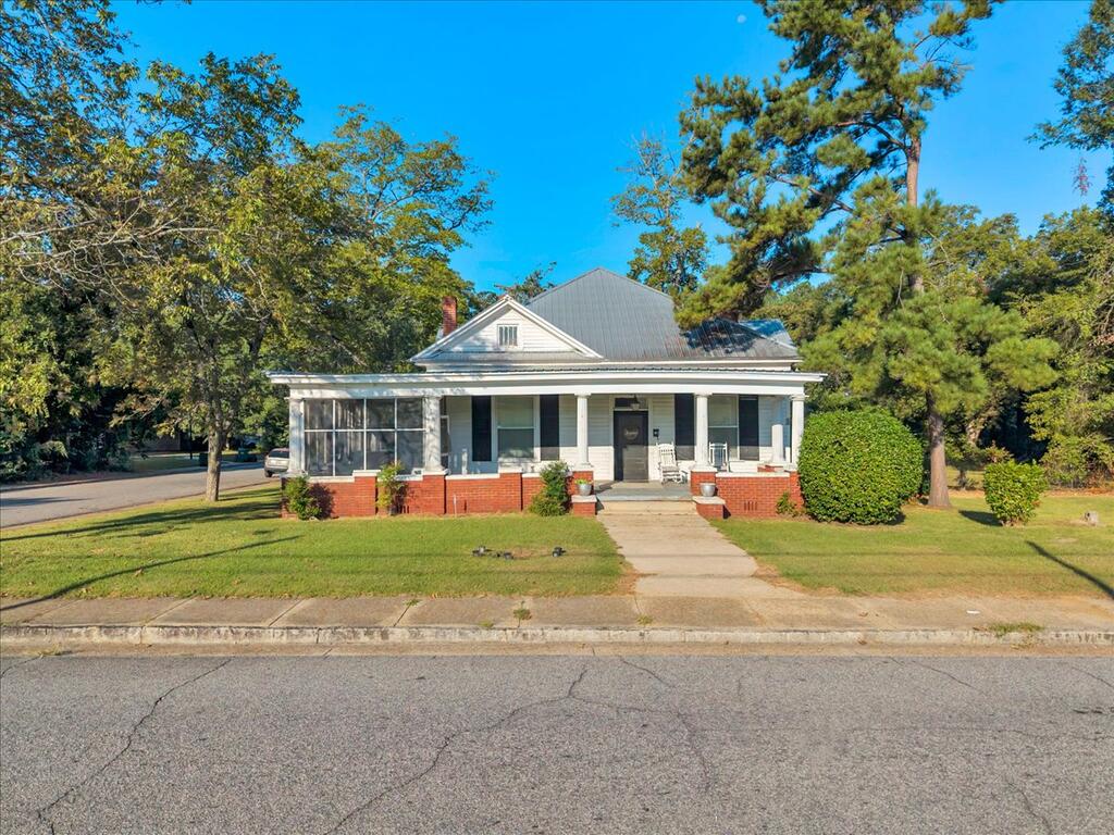 Single-story house with a columned front porch, screened porch, and red brick foundation.