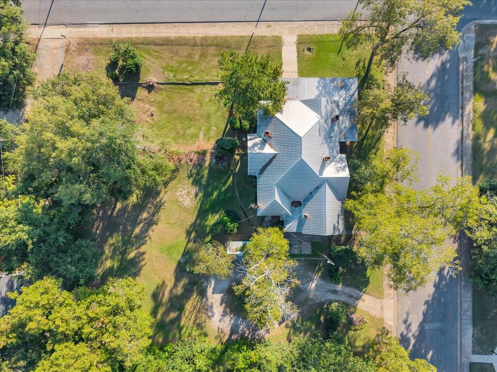 Aerial view of a house with a metal roof, surrounded by a large tree-lined yard.