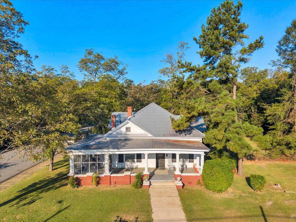 White and red-brick house with a metal roof, covered porch, and mature trees.