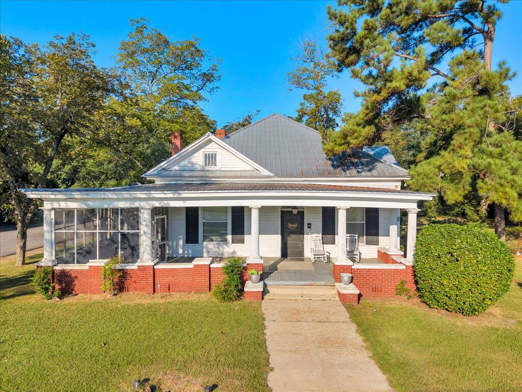House with a broad columned porch, gray metal roof, and red brick foundation.