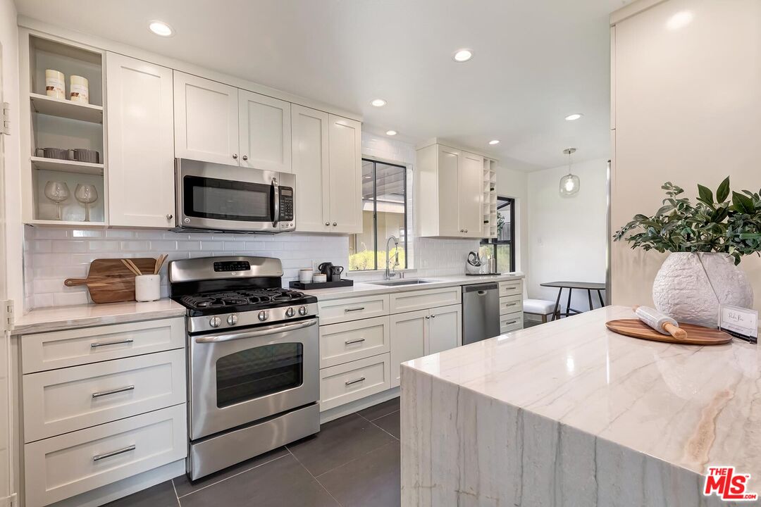 Kitchen with white shaker cabinets, stainless steel appliances, and a large marble island.