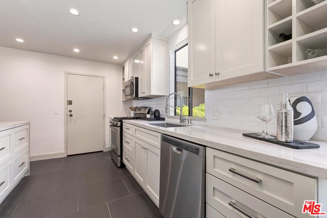 Renovated white kitchen with marble-look counters, stainless steel appliances, and a window above the sink.