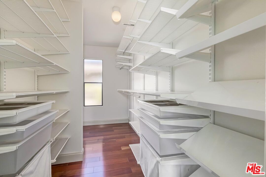 Walk-in closet with white shelving, storage bins, and reddish wood flooring.