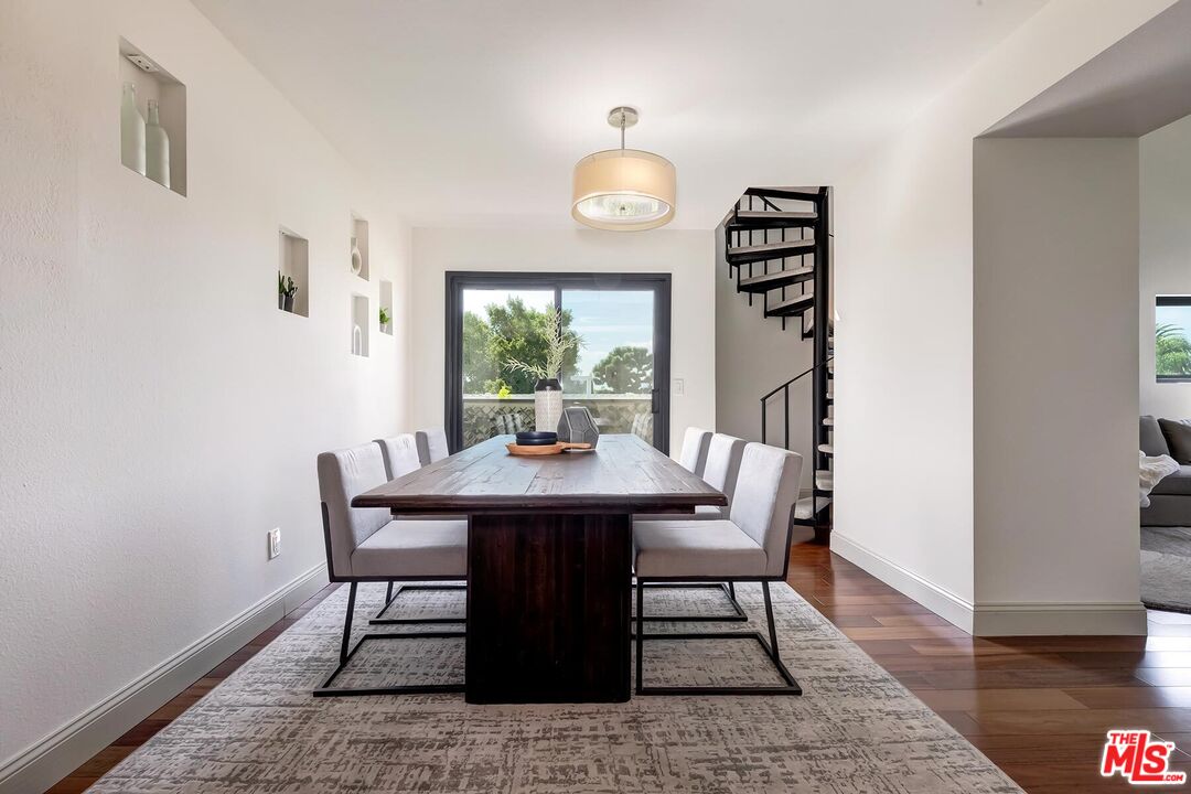 Dining room with a dark wood table, upholstered chairs, glass balcony doors, and a black spiral staircase.