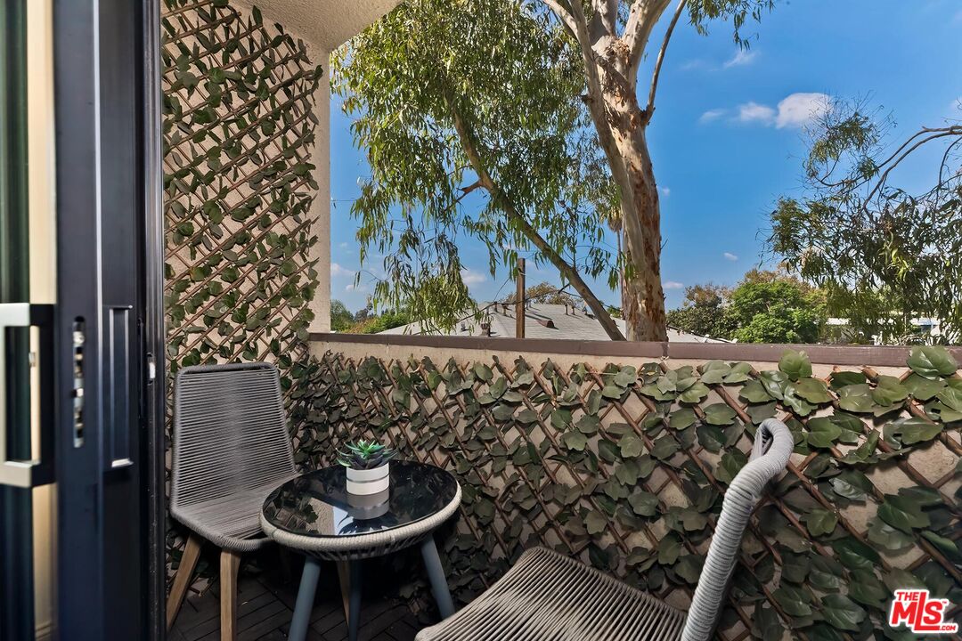 Apartment balcony with a bistro table, woven chairs, and leafy trellis screen.