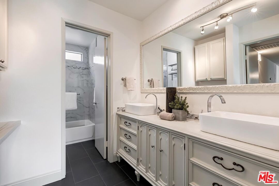 Bathroom with a double-sink vanity, large mirror, and marble-look tub surround.