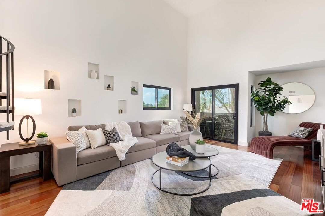 Living room with a gray sectional, round coffee tables, patterned rug, and balcony doors.