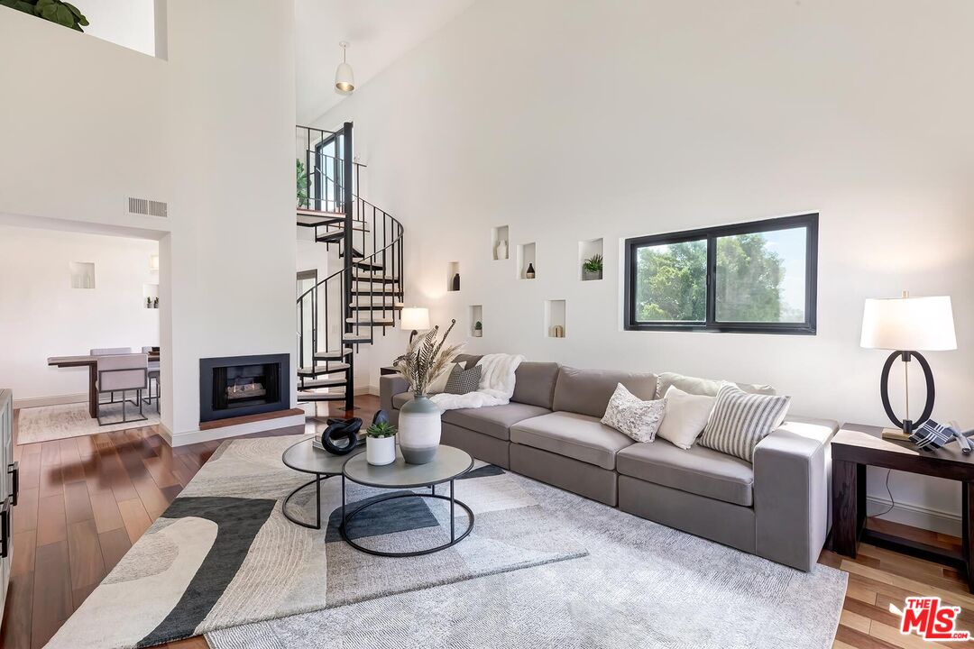 Living room with a gray sectional, black spiral staircase, fireplace, and high ceilings.