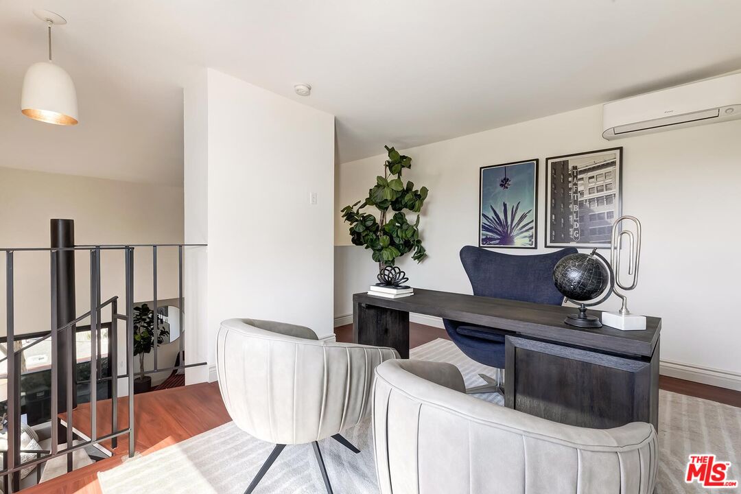Furnished home office with a dark desk, blue chair, and two white guest chairs beside a loft railing.