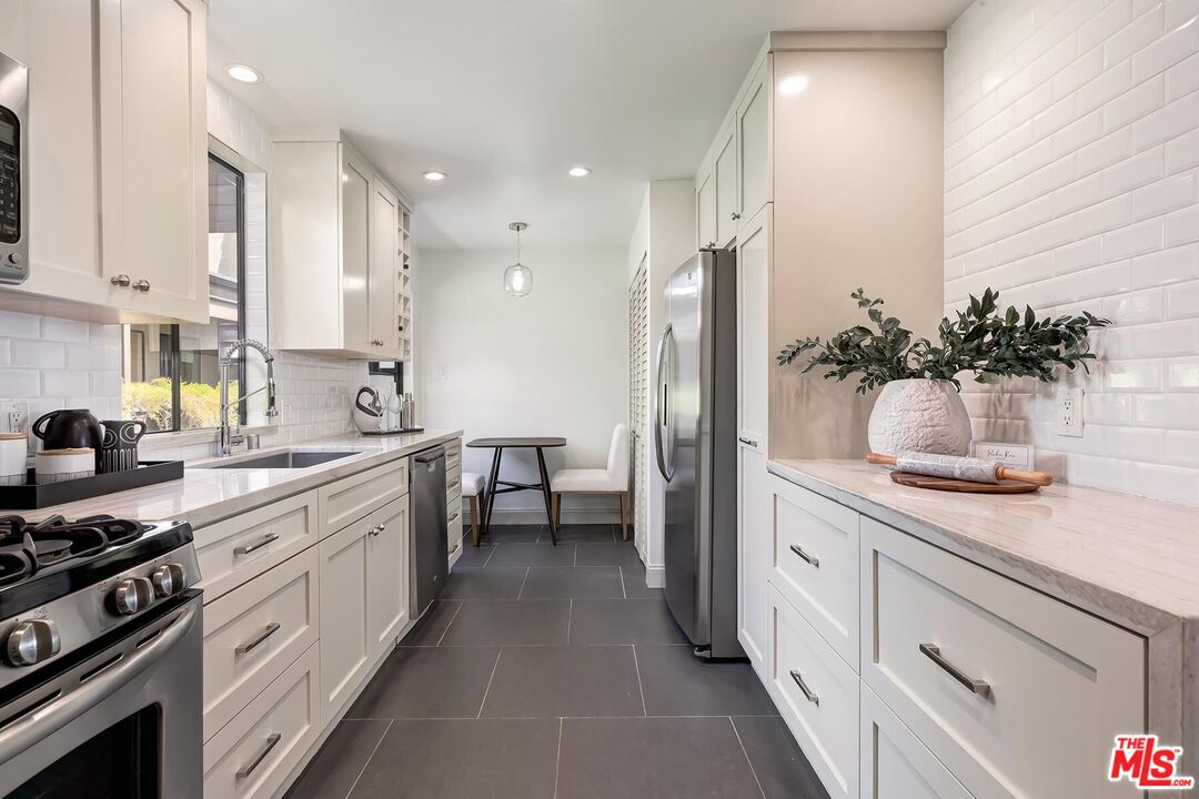 Galley kitchen with white cabinets, stainless steel appliances, and a small dining nook.