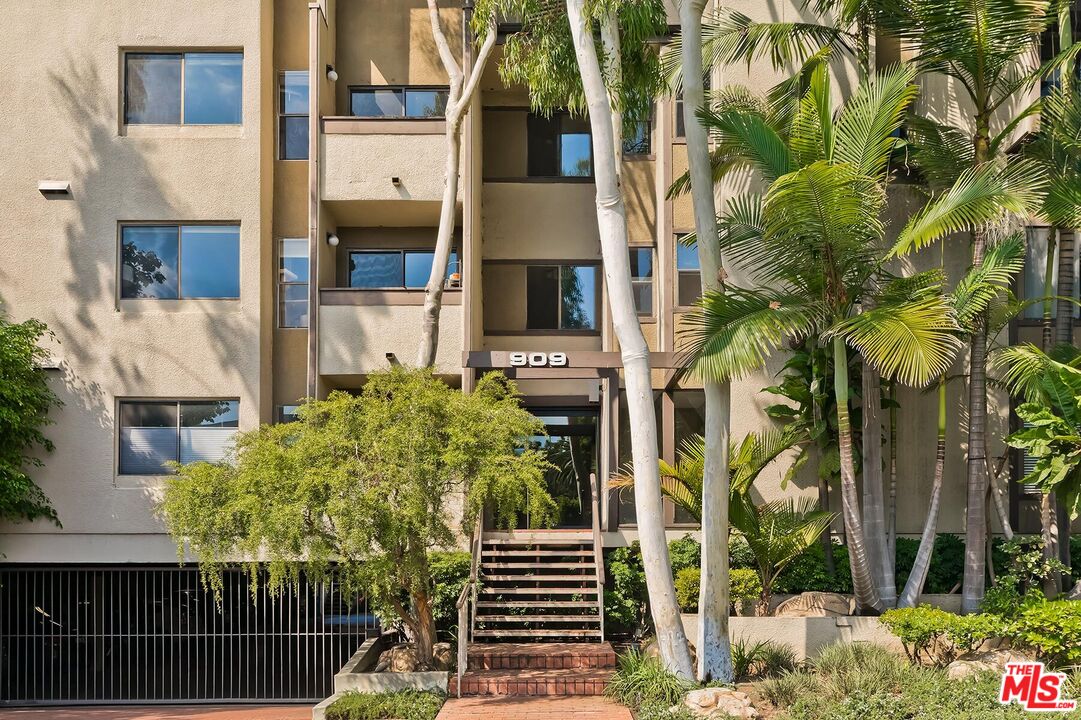 Condominium entrance marked 909, framed by palm trees and landscaped grounds.