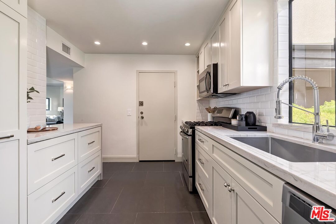Renovated galley kitchen with white cabinets, marble-look counters, and a large sink beneath the window.