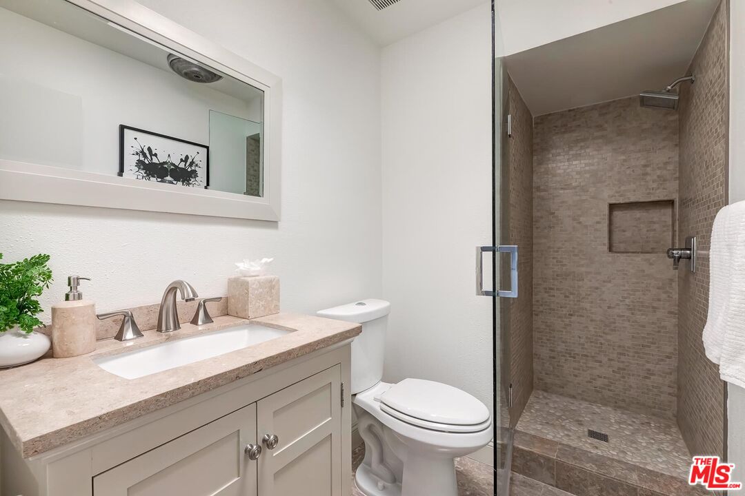 Bathroom with a pale stone vanity, white cabinetry, and a glass-enclosed taupe-tiled shower.