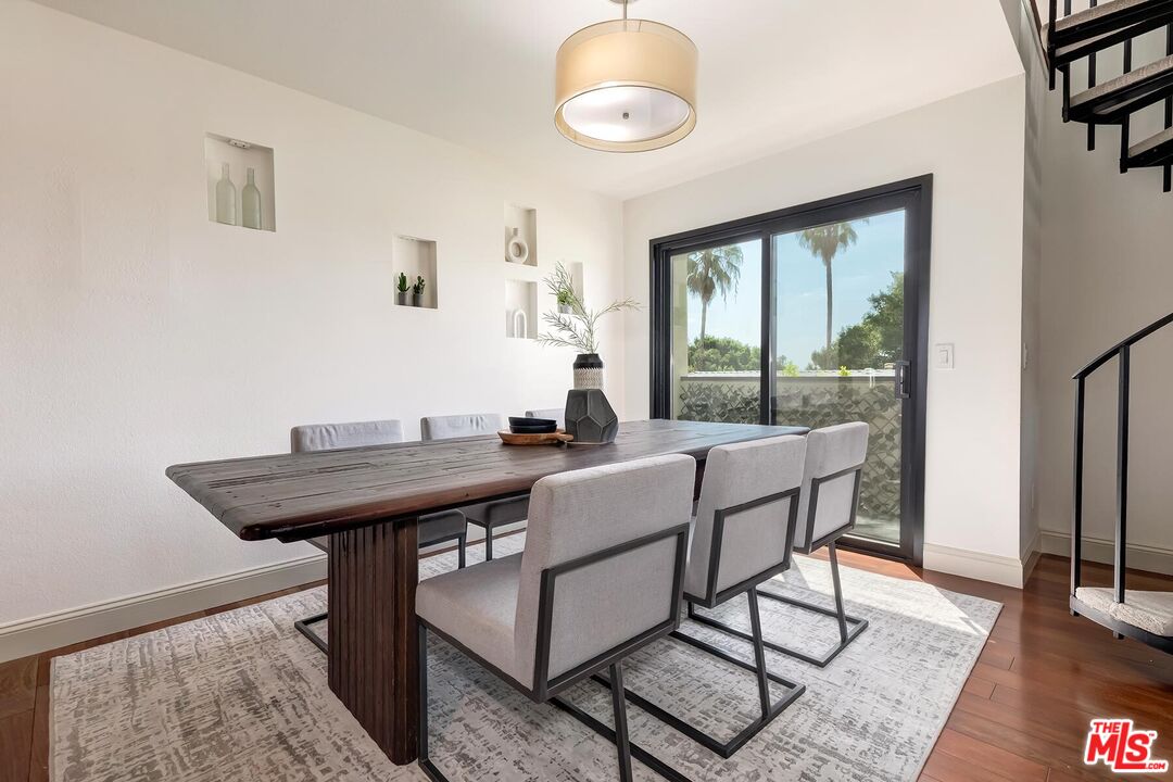 Dining room with a dark wood table, gray chairs, and sliding glass doors opening to a palm-lined view.
