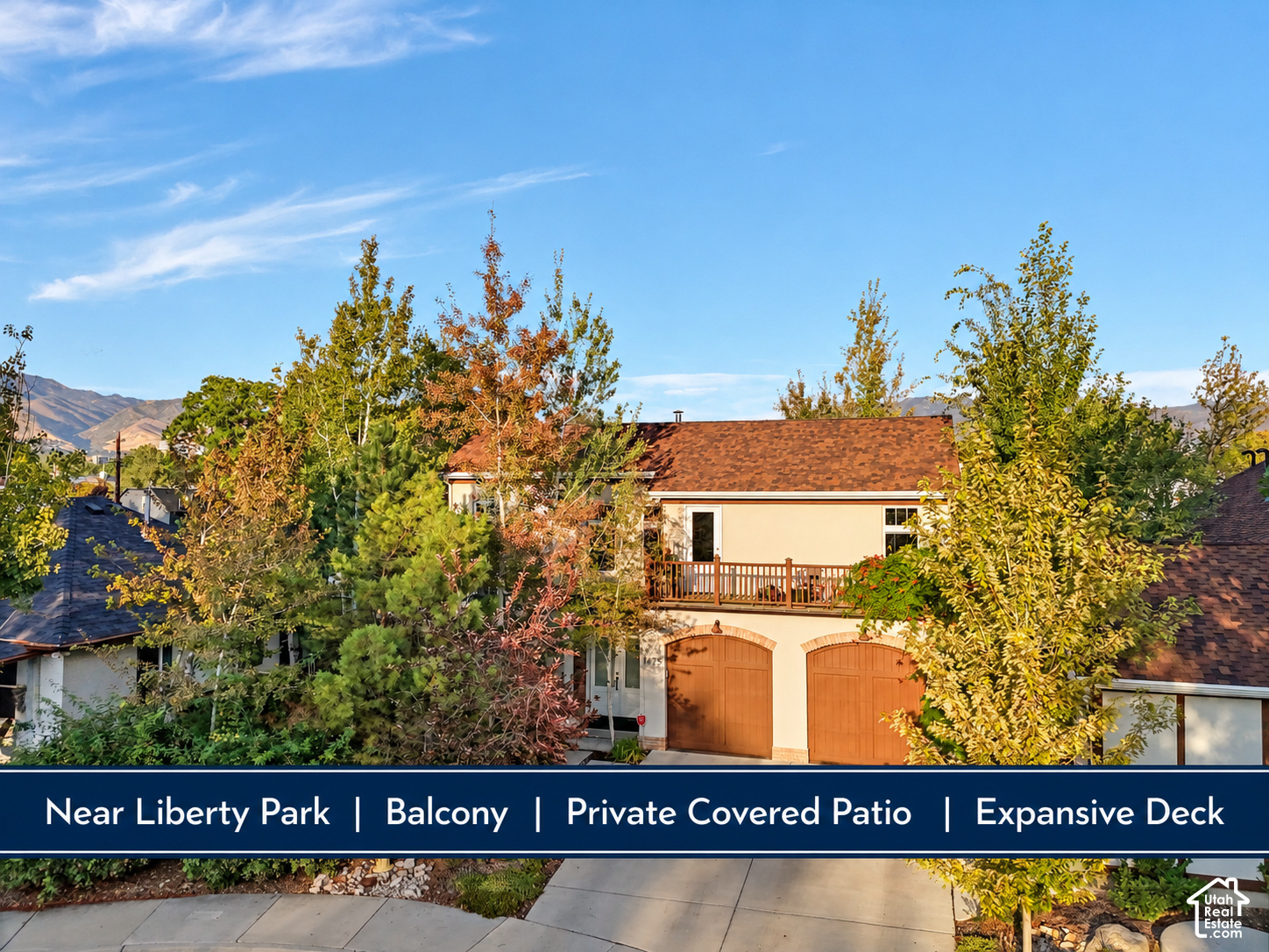 Two-story home with an upper balcony and arched garage doors, framed by autumn trees.