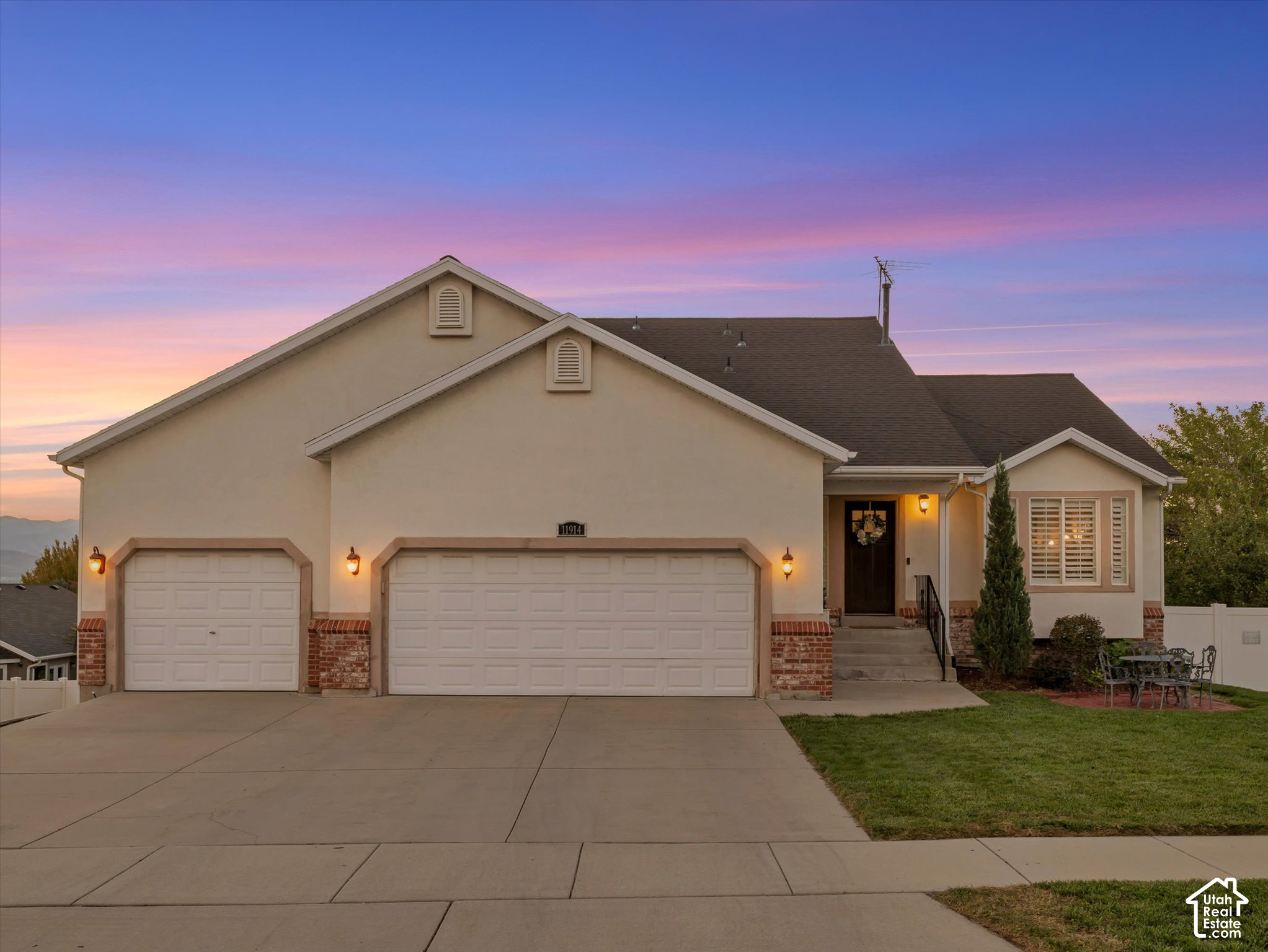 Beige stucco home with two garage doors and a small patio beneath a colorful dusk sky.
