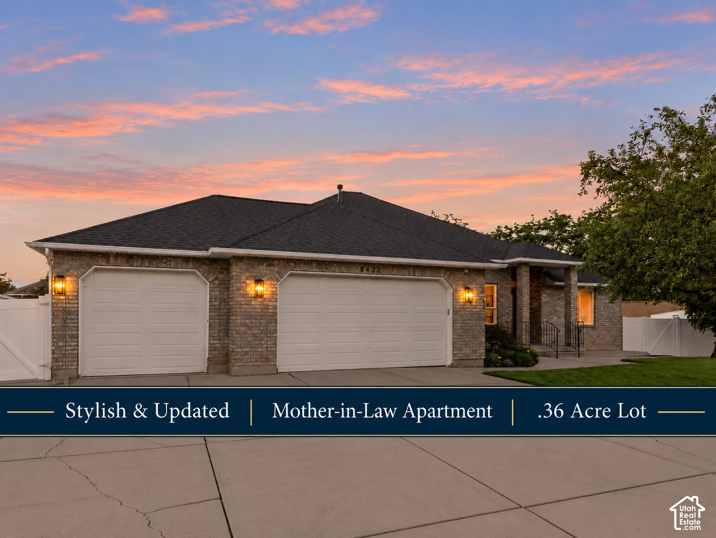 Brick home at dusk with two garage doors, white fencing, and a pink sunset sky.