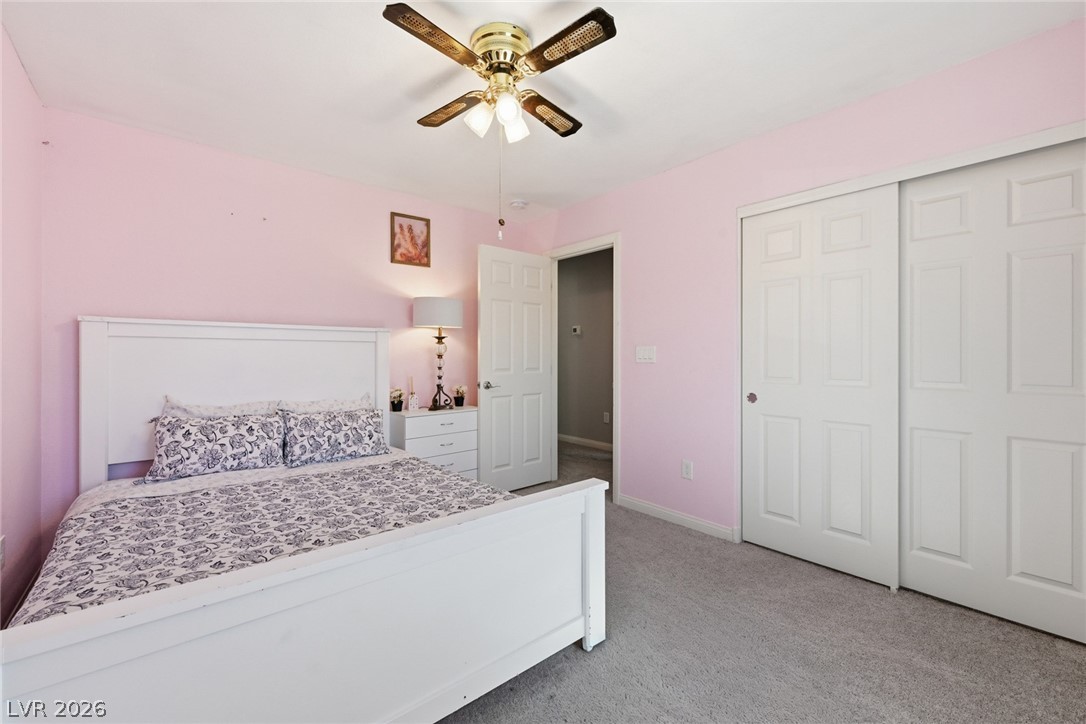 Bedroom with pink walls, a white bed with patterned bedding, and white closet doors.