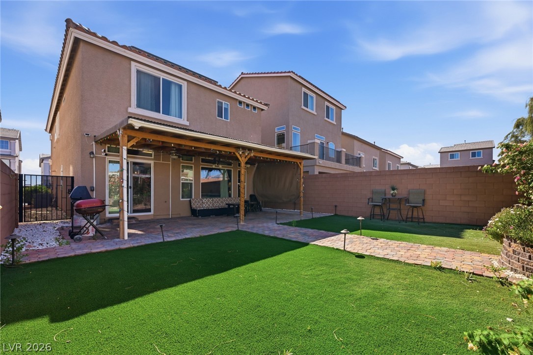 Two-story stucco home viewed from the backyard, with a covered patio and artificial grass lawn.