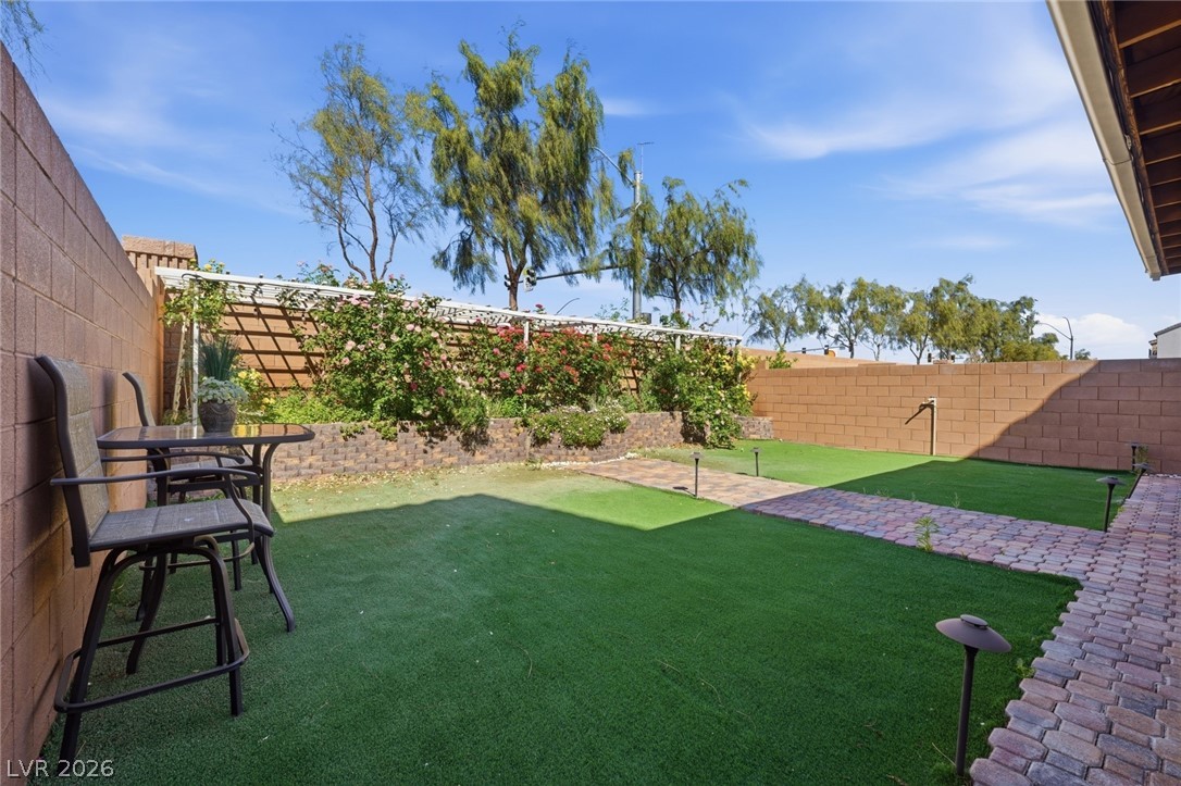 Enclosed backyard with green lawn, paver paths, flowering trellis vines, and outdoor seating.