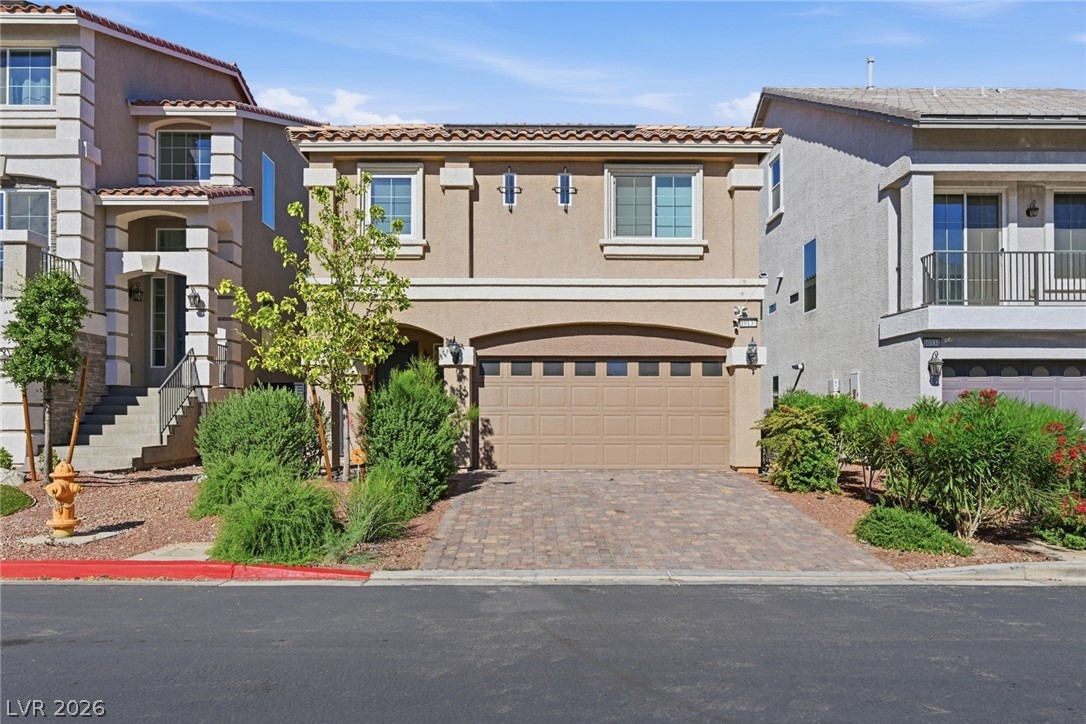 Two-story tan stucco home with a double garage, paver driveway, and landscaped front yard.