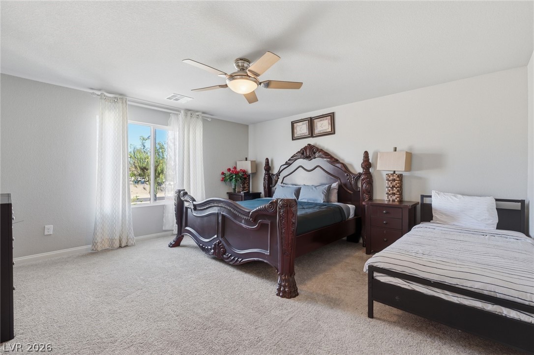 Furnished bedroom with an ornate dark wood bed, twin bed, beige carpet, and bright window.