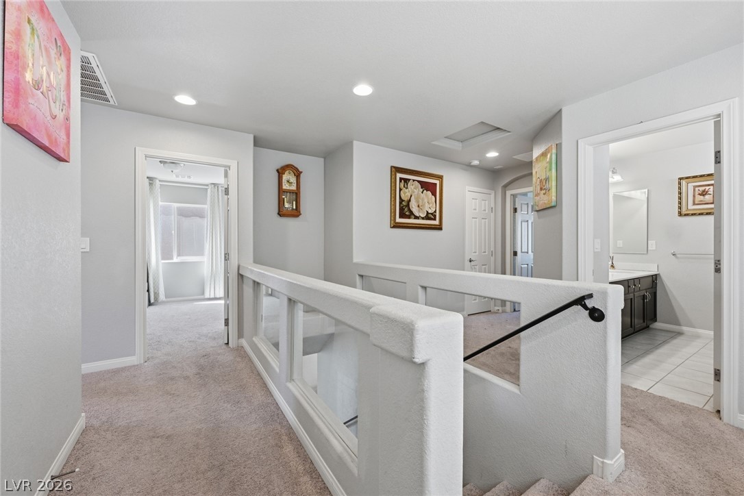 Upstairs hallway with a white stair railing, beige carpet, and open bedroom and bathroom doorways.