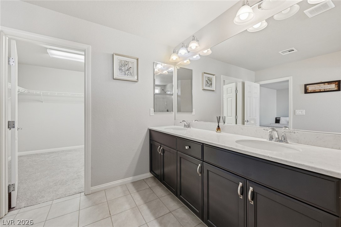 Bathroom with a double-sink vanity, dark cabinetry, and an open walk-in closet.