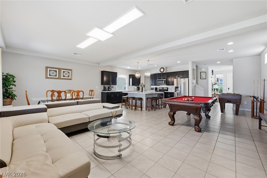 Open-plan game room with a red-felt pool table, cream sectional, and dark kitchen cabinetry.