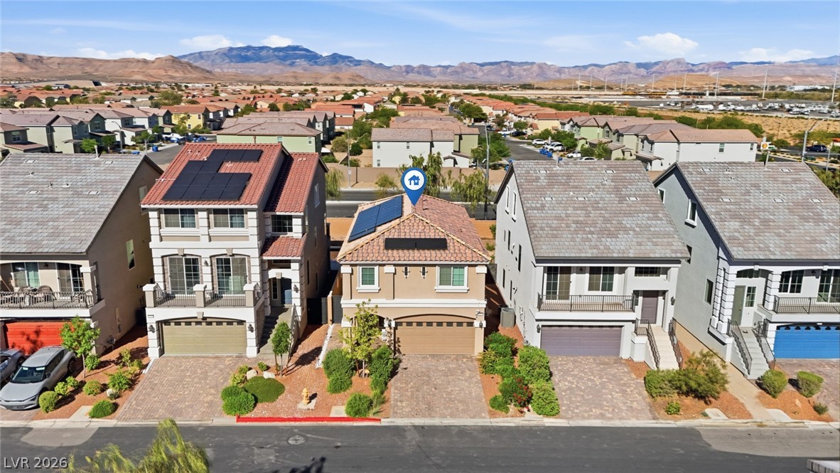 Two-story tan home with rooftop solar panels, neighboring houses, and distant mountains.