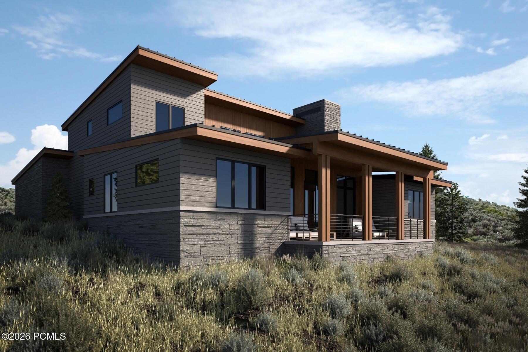 Modern two-story home with dark siding, stone accents, and a covered timber deck in a grassy meadow.