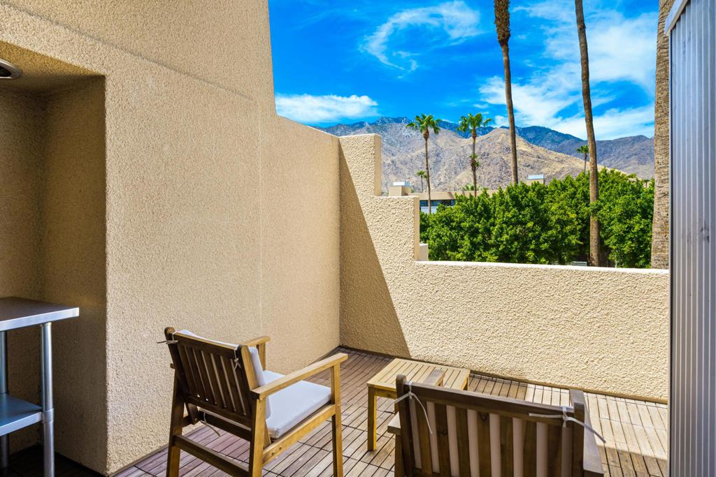 Private patio with wooden seating and mountain views beyond palm trees.
